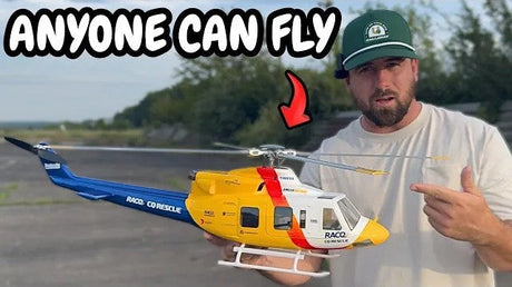 Man holding a yellow and blue RC helicopter outdoors.