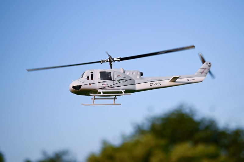 FLYWING UH-1 V4  giant RC helicopter in flight against blue sky and green trees