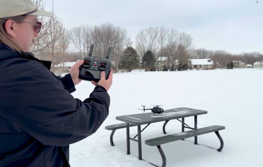 Adult pilot operating a YU XIANG MD500 Little Bird Military Helicopter outdoors in snow