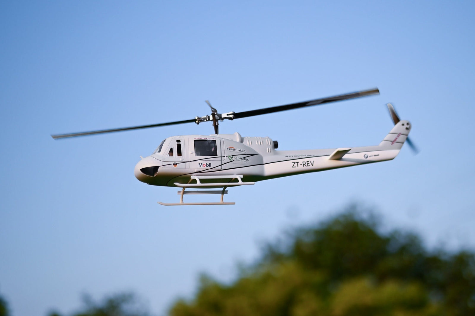 Large RC helicopter for adults flying against a clear sky, showcasing scale realism and performance