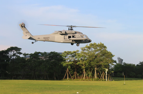 Scale rc helicopter in flight over a grassy field with trees